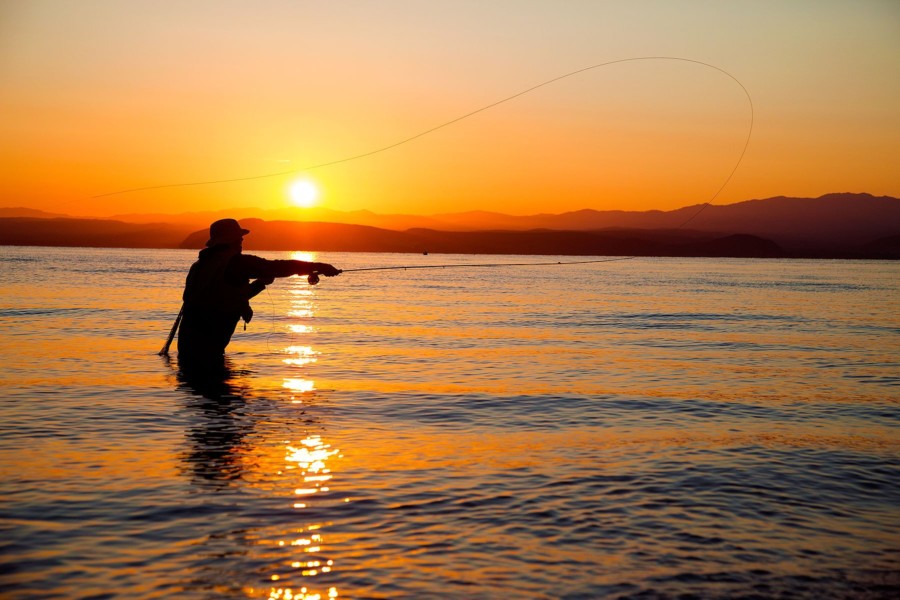A man fishing with a sunset in the background